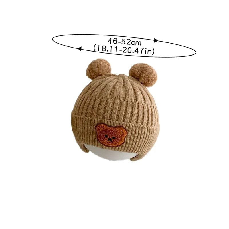 Brown knit baby hat with bear face design and pom-poms on a white background