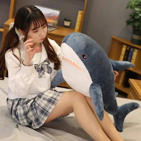 Person holding a large shark plush toy in a room with a desk and books.