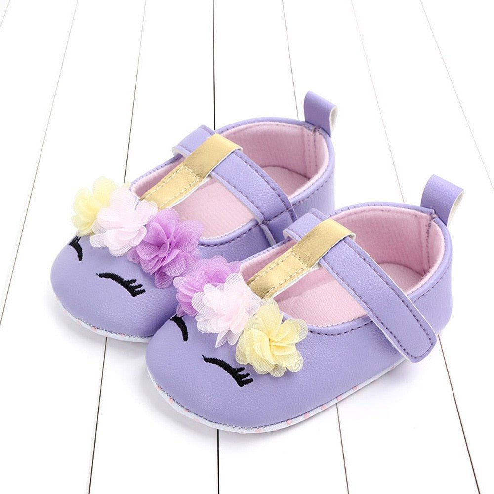 Purple baby shoes with floral decorations on a white wooden floor