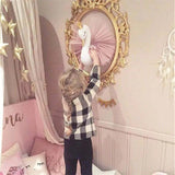 Child playing with a toy swan in front of a decorative mirror in a pink-themed room.