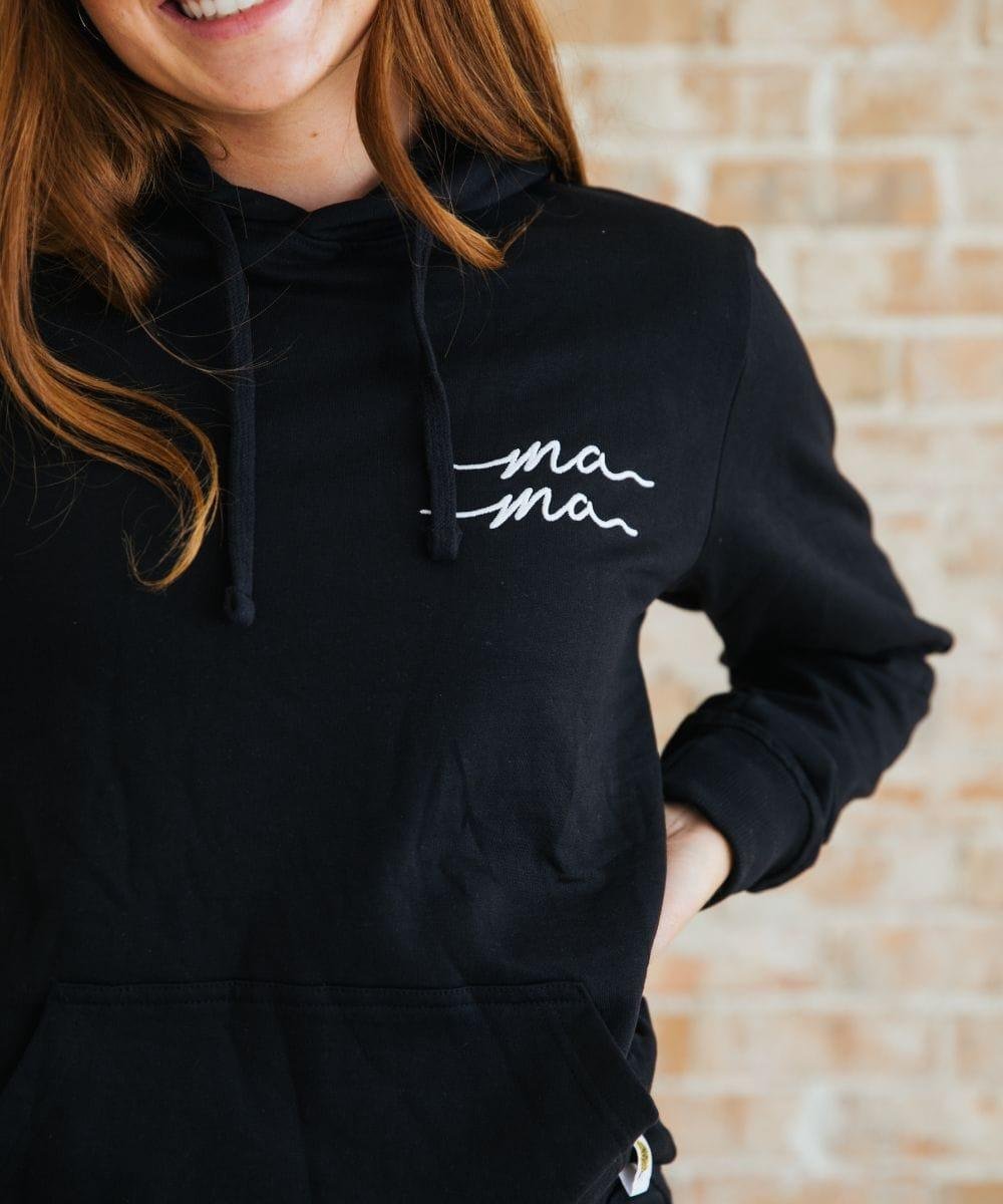 Person wearing a black hoodie with 'mama' text, standing against a brick wall.