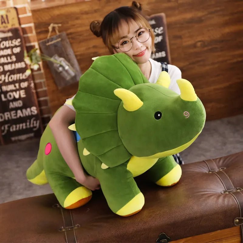 Person holding a large green dinosaur plush toy in a cozy indoor setting.