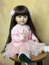 Realistic doll with long dark hair and a pink dress sitting on a wooden stool.