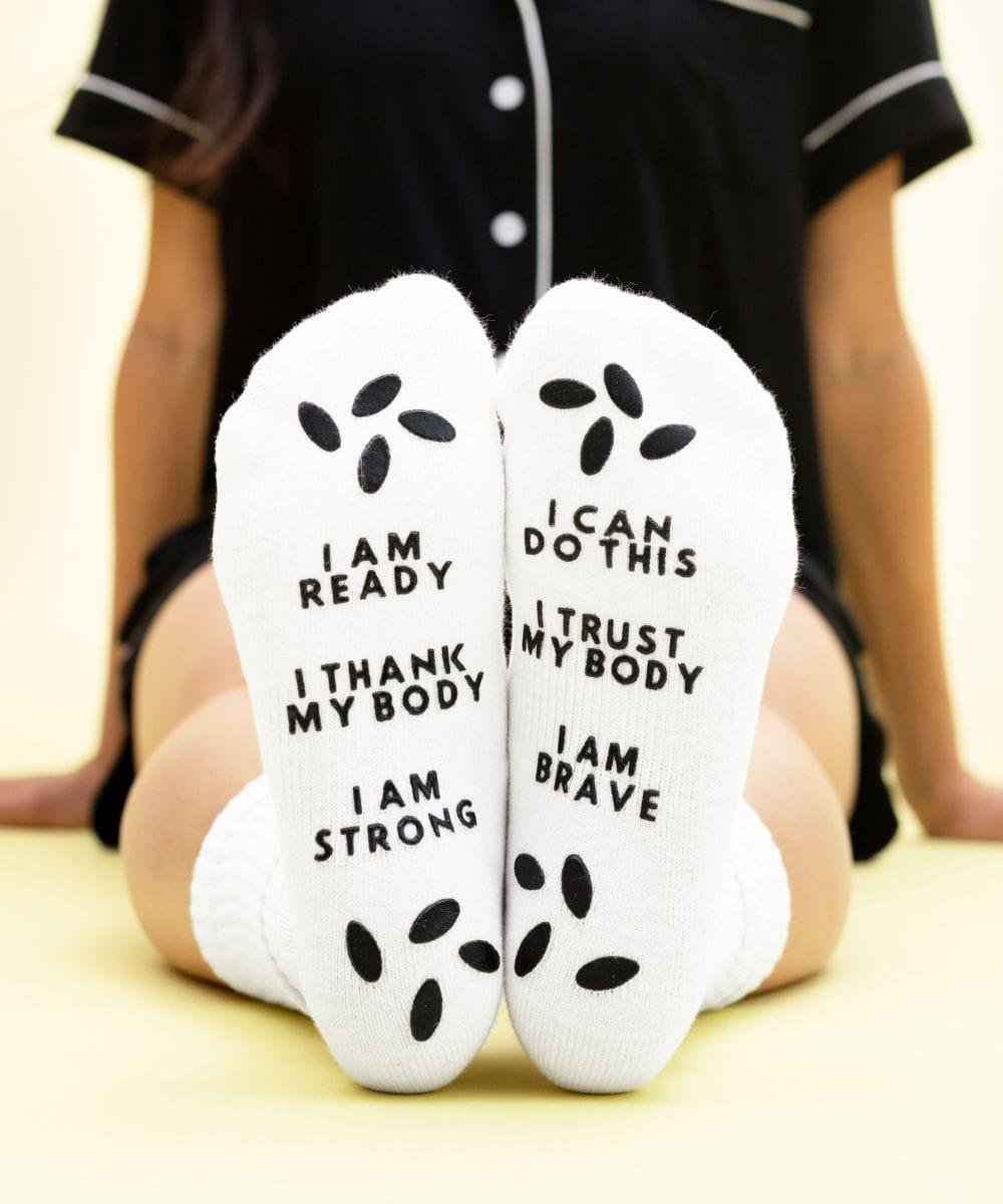 White socks with motivational text worn by a person sitting on a light-colored floor.