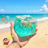 Clear cube with blue jelly-like substance filled with small toys and decorations.
