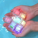 Colorful glowing ice cubes held in hands with a blue water background