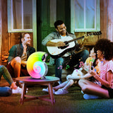 Group of people sitting on a porch with a person playing guitar and a colorful robot on a table.