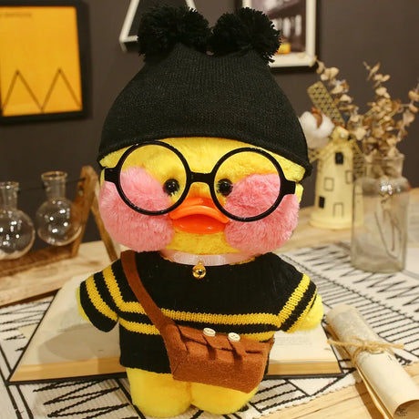 Plush toy duck wearing glasses, a black hat, and a black sweater with yellow stripes on a decorative surface.