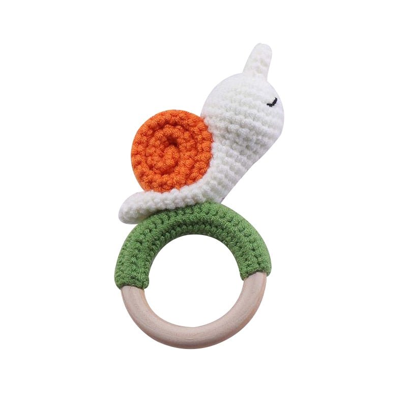 Crocheted snail rattle toy with orange shell, white body, and green base on a white background