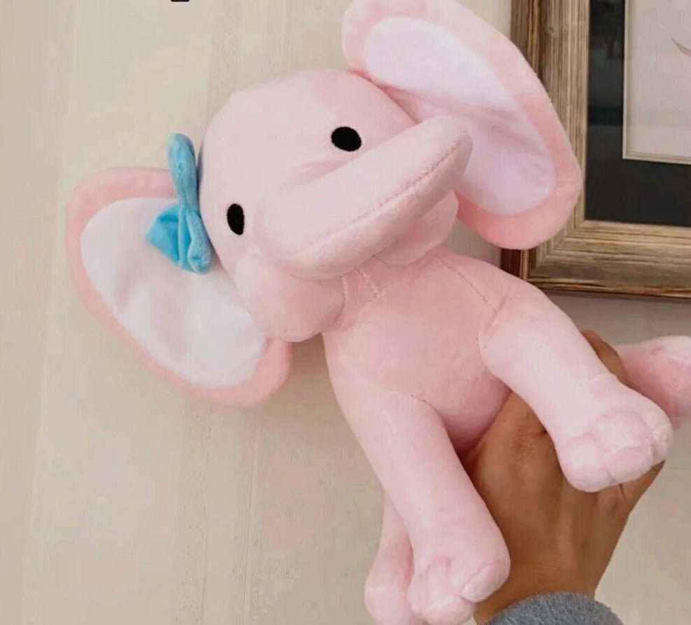Pink plush elephant toy with a blue bow held by a hand.