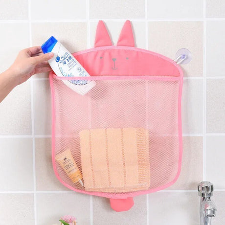 Pink mesh storage bag with bunny ears holding bath products on a tiled bathroom wall.