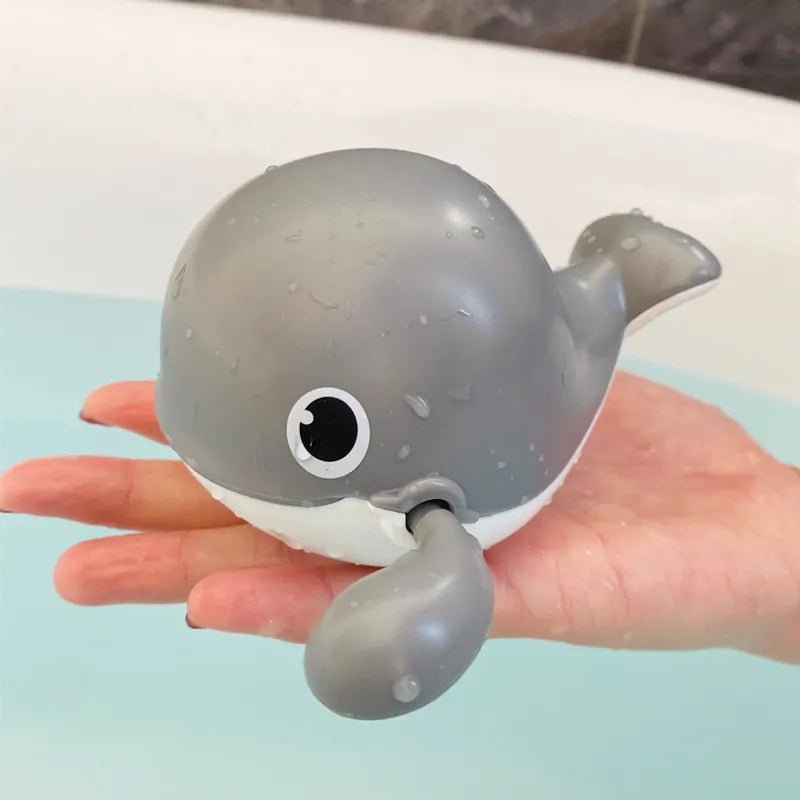 Gray whale-shaped bath toy held in a hand with a bathtub.