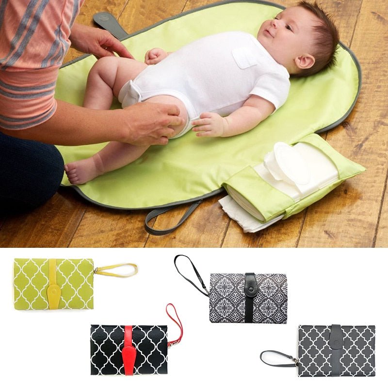 Baby lying on a green changing mat with a diaper bag.