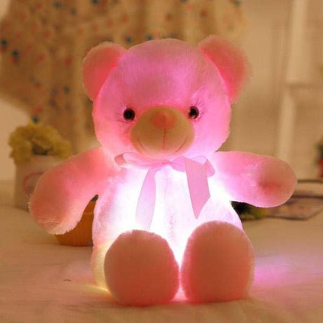 Pink LED teddy bear on a bed.