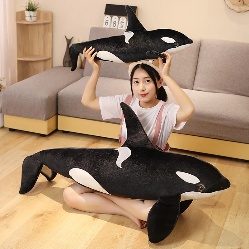 Person holding a large plush orca whale toy in a living room.