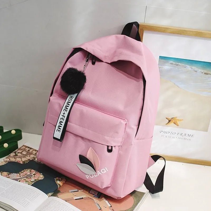 Pink backpack with a black pom-pom and visible brand logo on a surface.