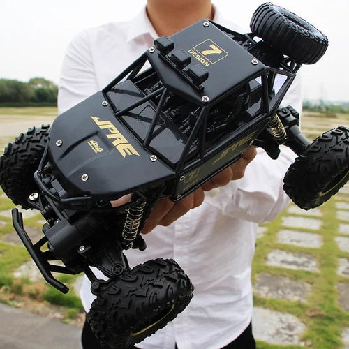 Person holding a black and gold remote control car with 'JPTK' branding outdoors.