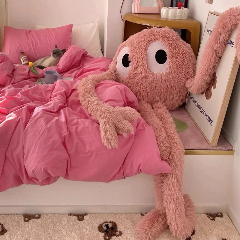 Pink plush octopus toy on a bed with pink bedding in a cozy room.