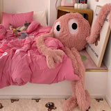 Pink plush octopus toy on a bed with pink bedding in a cozy room.