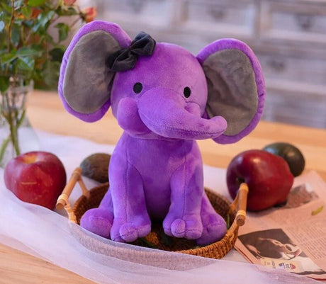 Purple elephant plush toy with a bow on a table with fruits