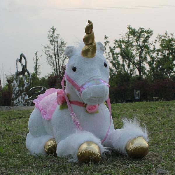 Plush unicorn toy with gold hooves and a pink saddle on grass
