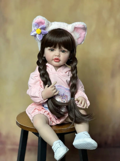 Doll with cat ears and a pink outfit sitting on a stool against a brown background