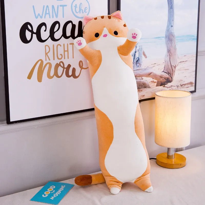 A cat-shaped plush toy in a room with a lamp and a framed picture on the wall.