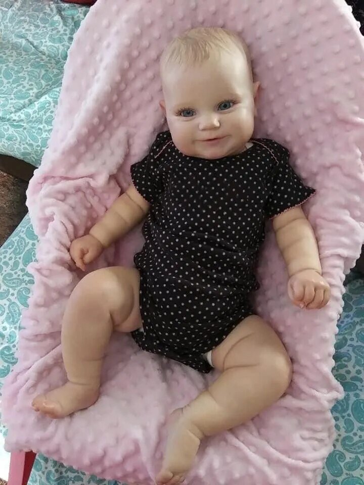 Baby doll in a black polka dot outfit lying on a pink cushion