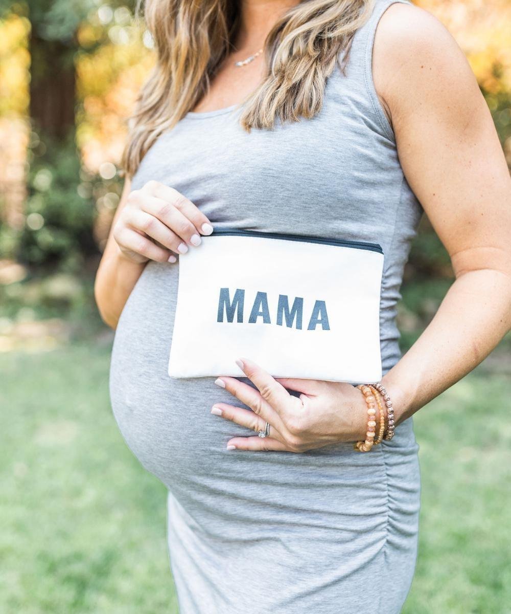 Pregnant person holding a sign that says 'MAMA' outdoors.