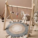 Children's play area with a wooden climbing frame, round rug, and hanging toys.