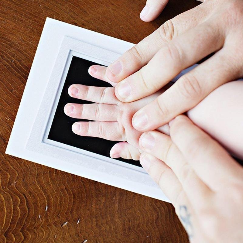 Close-up of a baby's hand pressed against a white frame on a wooden surface