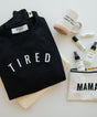 Black sweatshirt with 'TIRED' text, mug, and skin care products.
