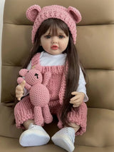 Doll wearing a pink outfit with a teddy bear and matching hat, sitting on a brown surface.