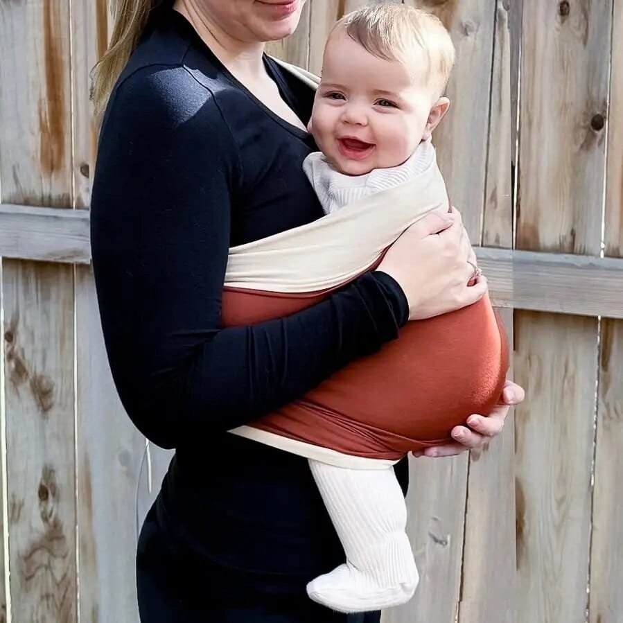 Woman holding a baby in a baby carrier against a wooden fence.
