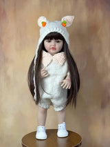 Doll wearing a knitted outfit with bear ears on a wooden stand against a brown background