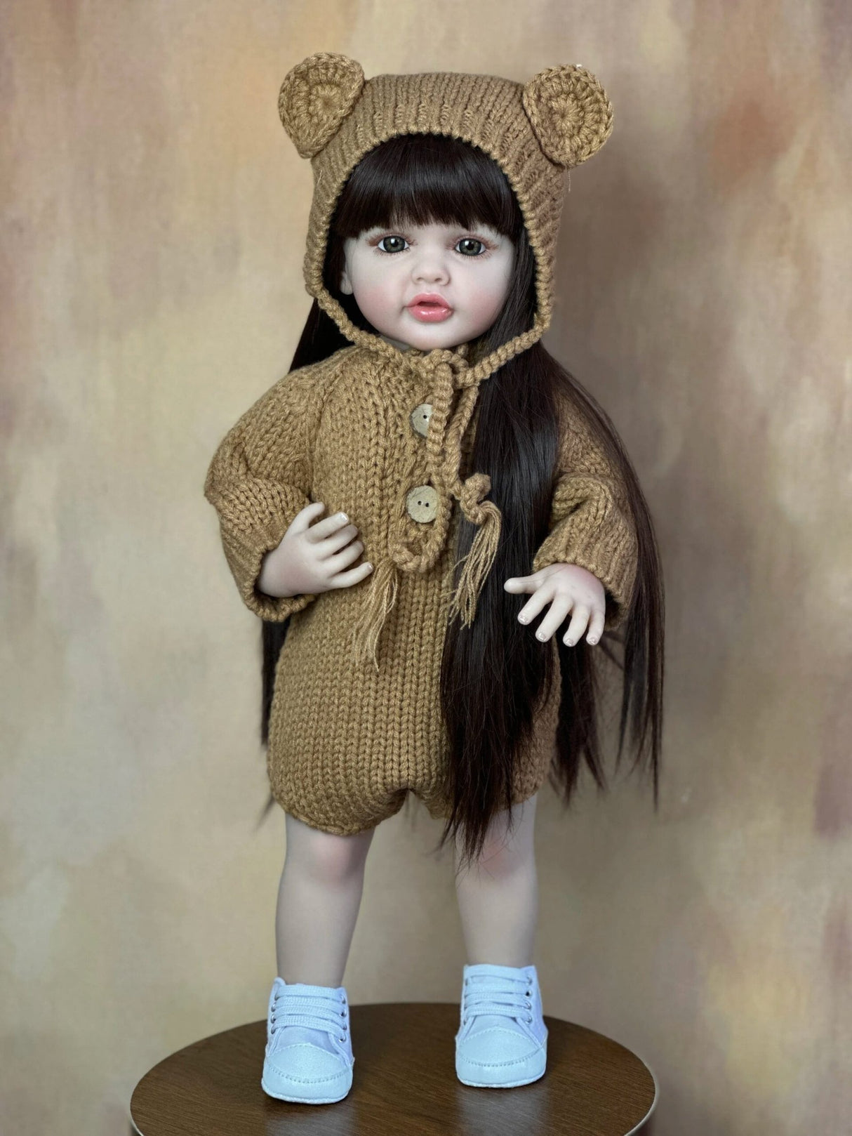 A doll wearing a brown knitted outfit with bear ears