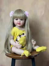 Doll with long blonde hair and a yellow outfit sitting on a small round table against a plain background.