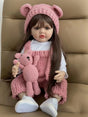 Doll wearing a pink outfit with a bear toy, sitting on a brown surface.