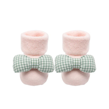 Pair of baby booties with pink fuzzy tops and green checkered bows on a white background