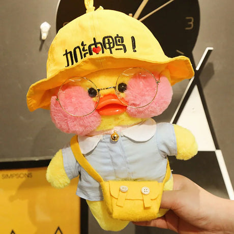 Plush toy resembling a duck wearing a yellow hat with text, glasses, and a denim outfit.