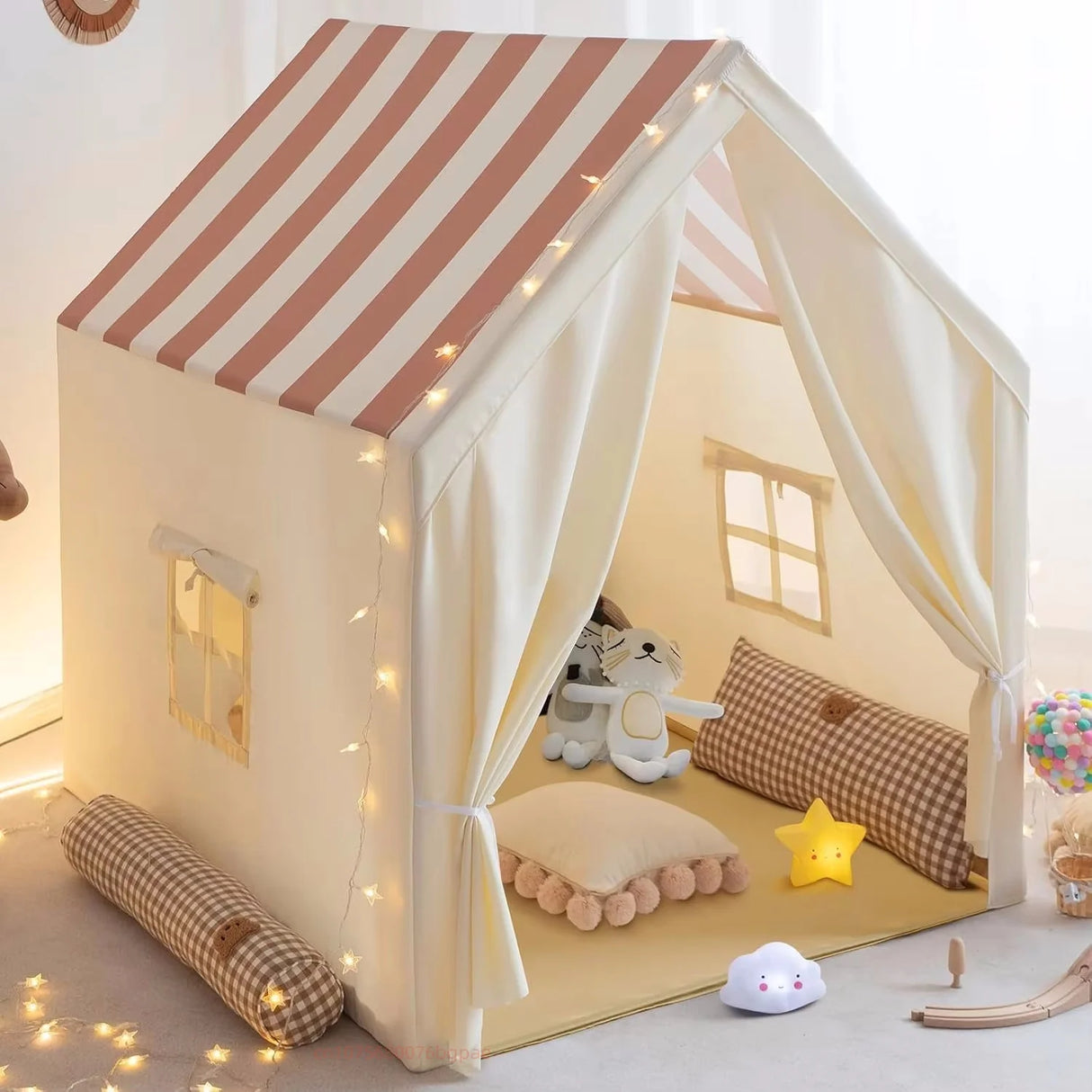 Children's play tent with striped roof, toys, and decorative lights in a room.