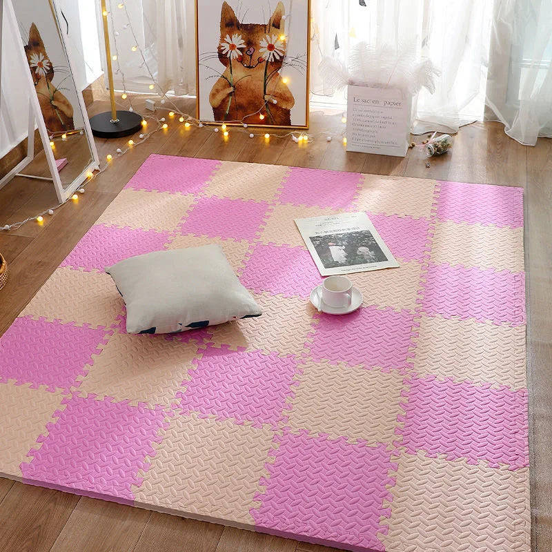 Pink and beige checkered foam mat on a wooden floor with a pillow and cup.
