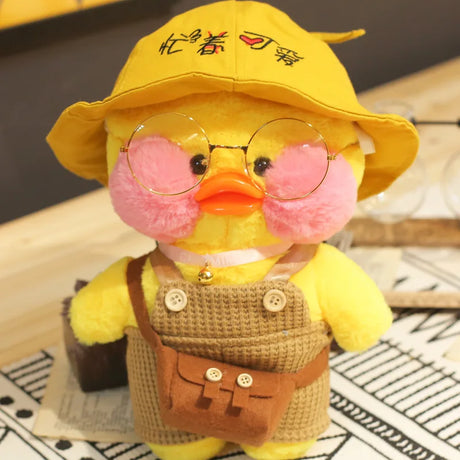Yellow plush duck toy with a yellow hat, pink cheeks, and a brown apron on a patterned surface.