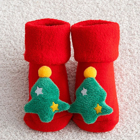 Red baby booties with green Christmas tree designs on a textured surface