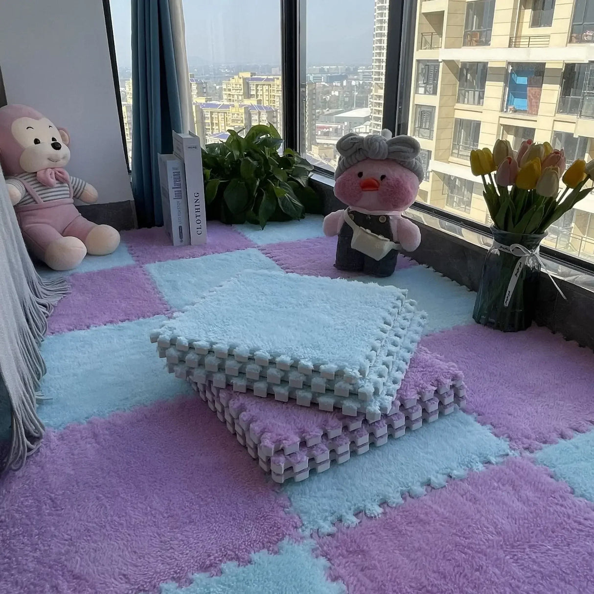 Colorful foam mats on the floor with plush toys and a vase of tulips near a window.