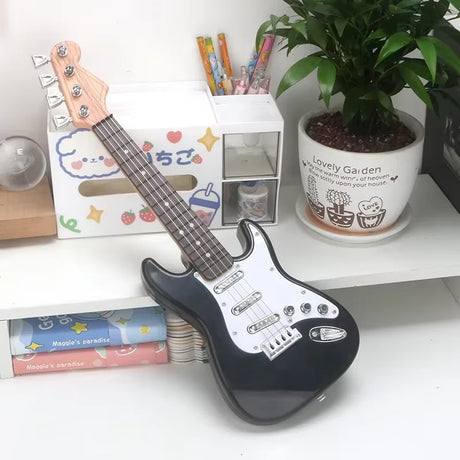 Black electric guitar on a white surface with stationery items and a plant in the background