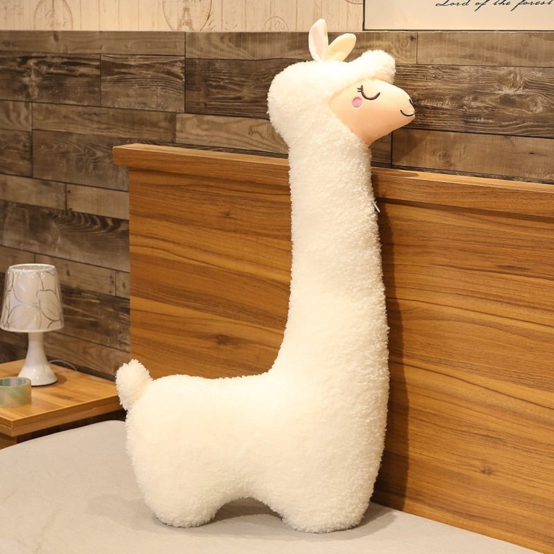 Plush llama toy against a wooden wall with a lamp on a shelf.