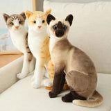 Three plush cat toys in different colors on a light surface.