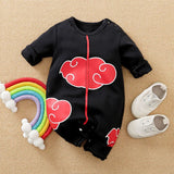 Black baby romper with red cloud designs on a beige surface, accompanied by a colorful rainbow toy and white shoes.
