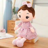 Plush toy doll with brown hair and a pink dress sitting on a wooden surface.